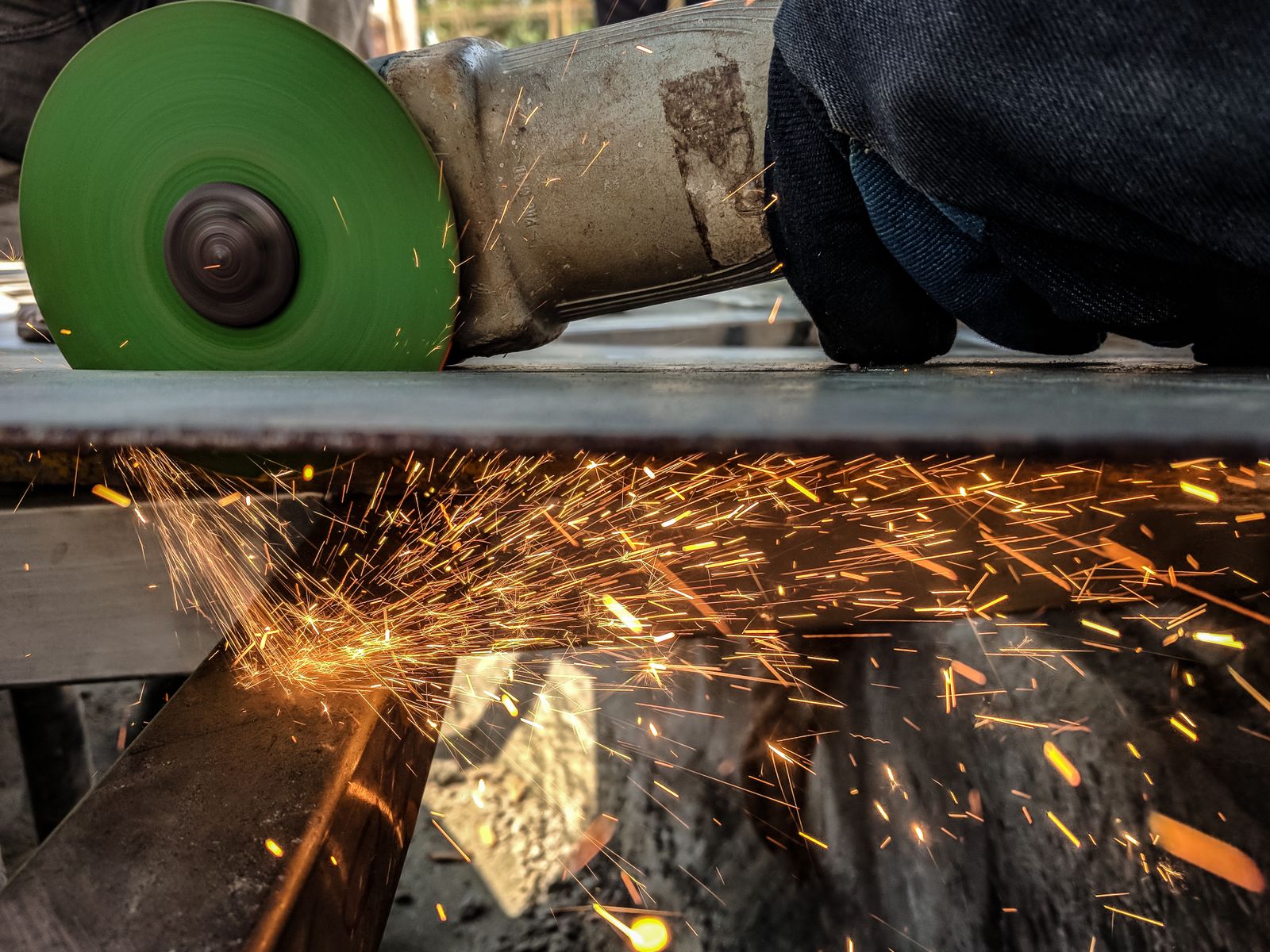 Person using a handheld angle grinder to cut a sheet of metal, throwing sparks