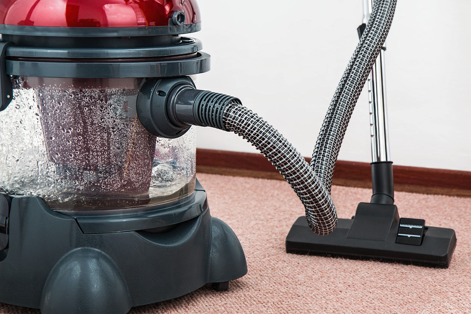 Red canister vacuum cleaner with hose and floor nozzle resting on carpet