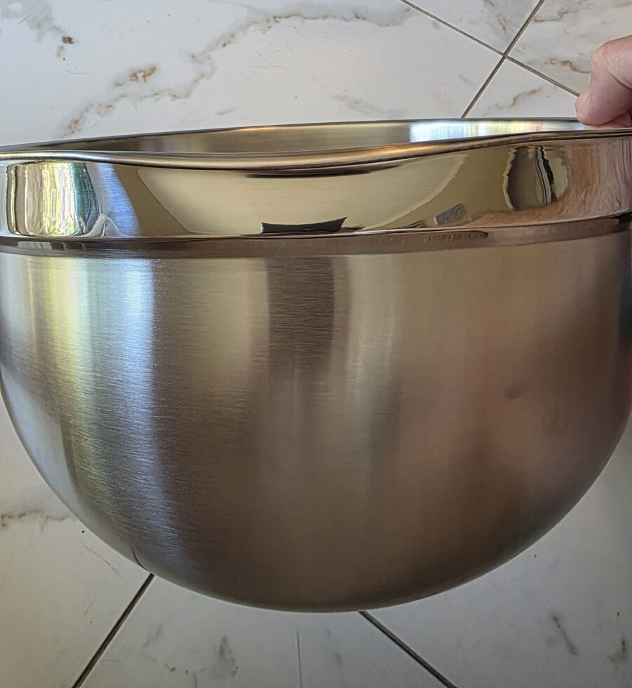 Closeup of a stainless mixing bowl's polished rim showing a visible bend from shipping damage
