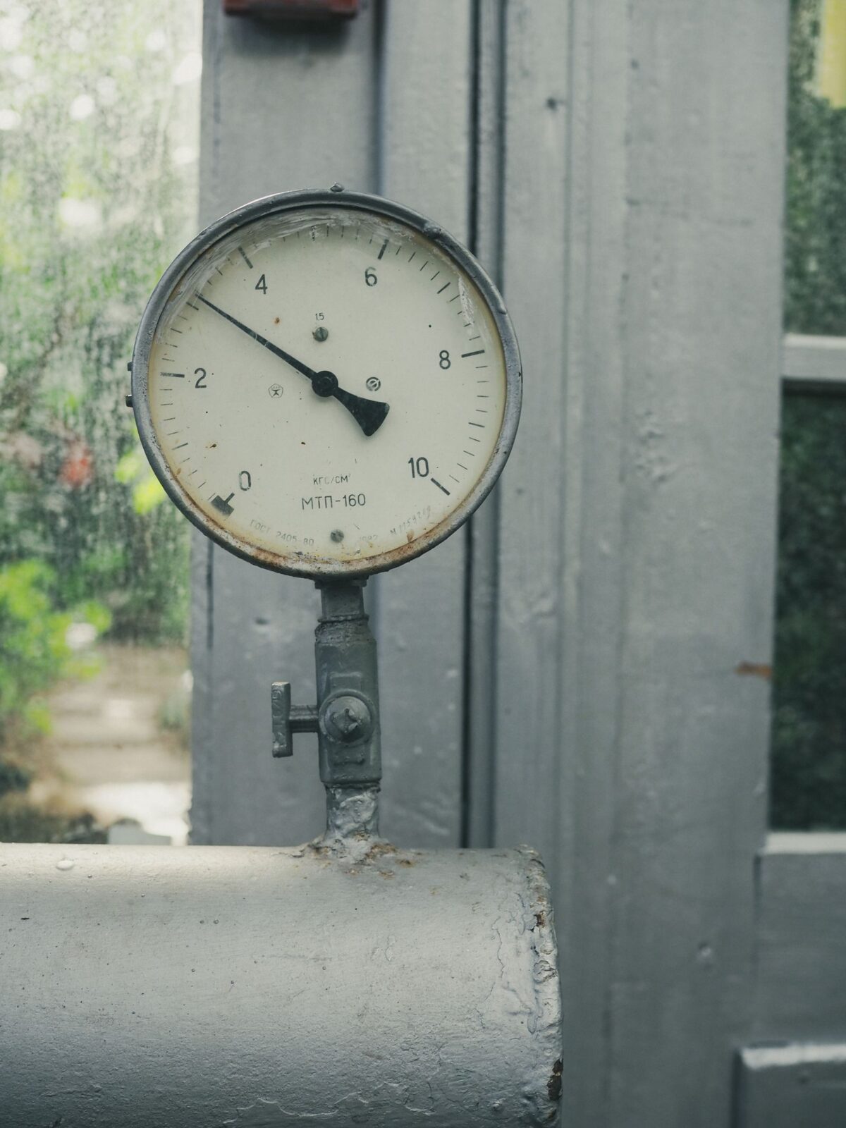 Round dial pressure gauge with a needle mounted on a gray pipe