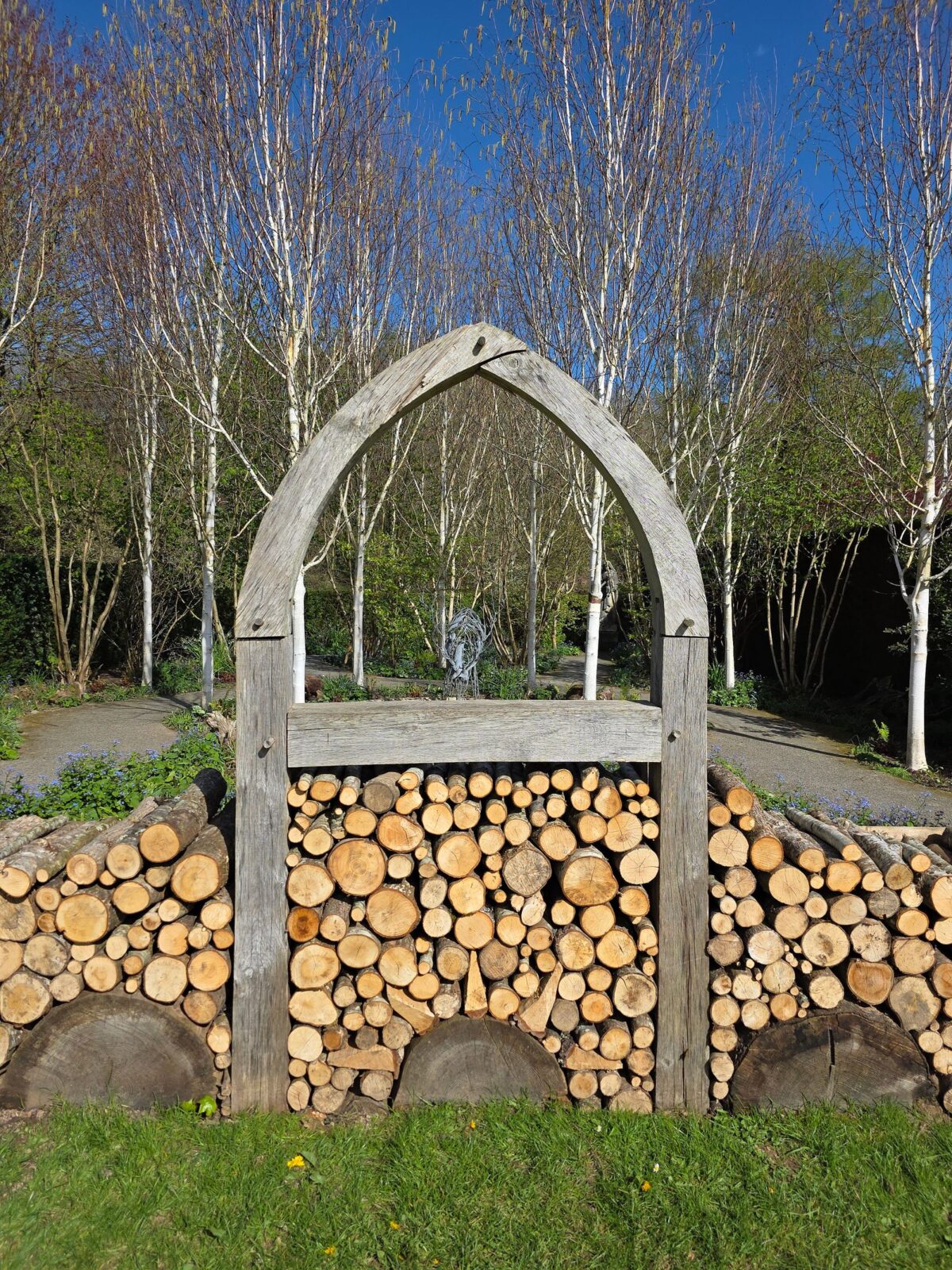 Split logs stacked in a wooden arch frame on thick round log slabs above the grass
