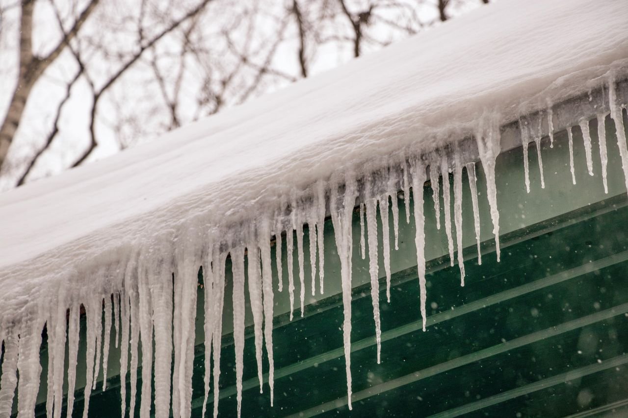 Icicles hanging from the snow-covered edge of a roof above green siding