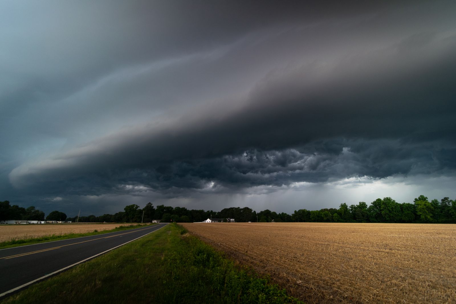 A dark shelf cloud rolling over a country road and open fields