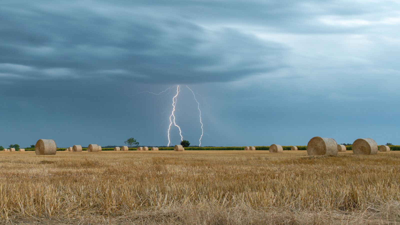 Lightning over a stubble hayfield dotted with round bales