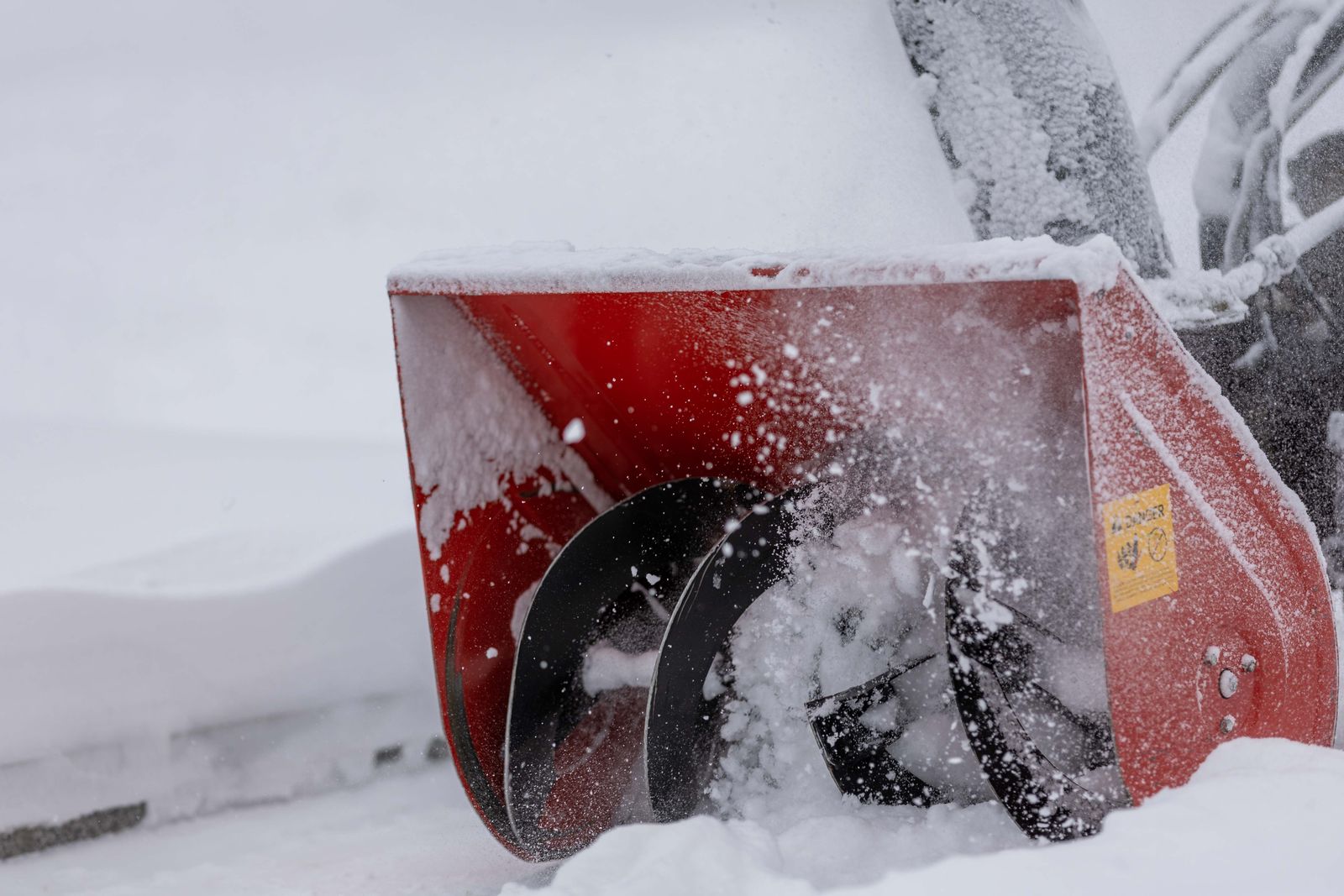 Close-up of a red single-stage snow blower auger housing churning through fresh snow