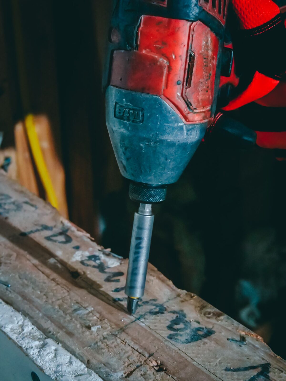 Red cordless impact driver with a bit driving into a rough wood board