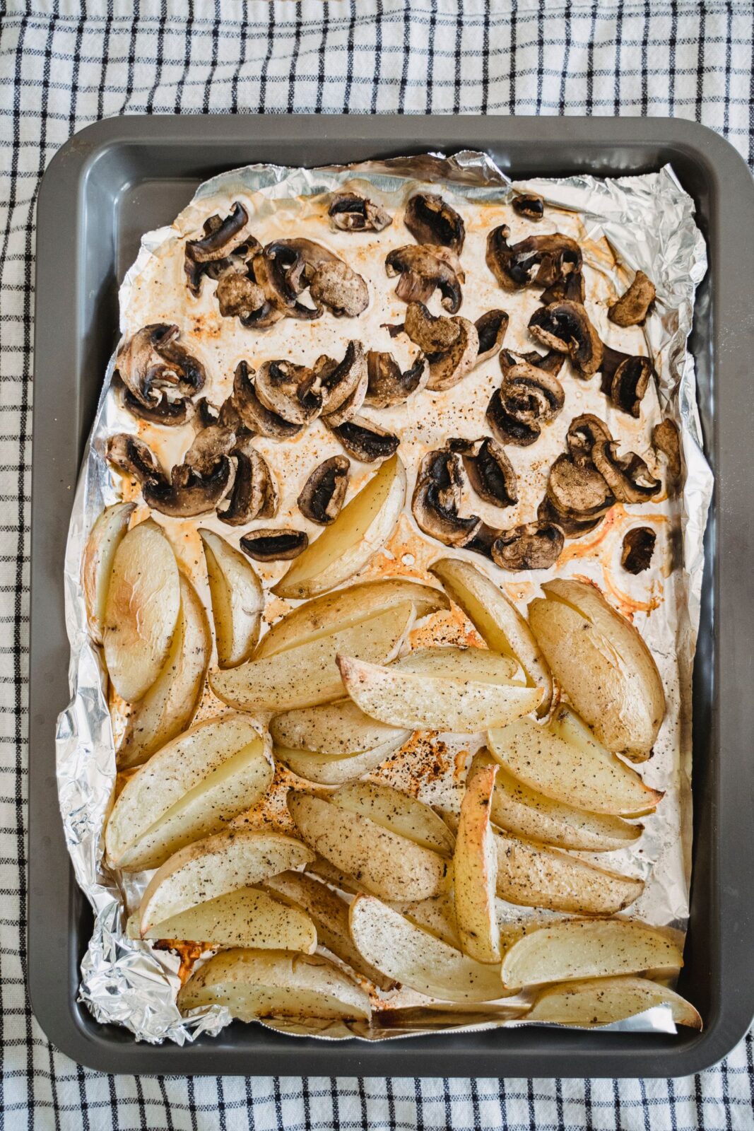 Roasted potato wedges and mushrooms on a foil-lined metal baking tray