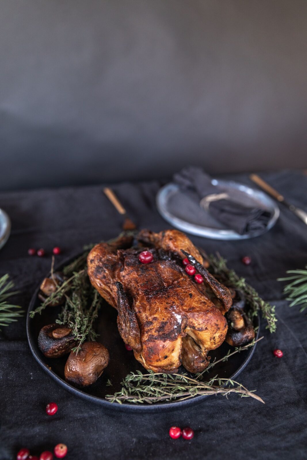 Whole roasted bird on a black plate with thyme sprigs, mushrooms and cranberries