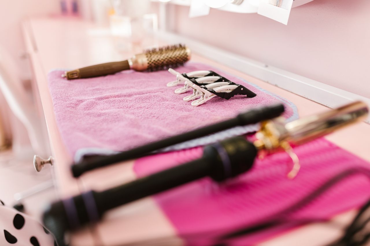 Round brushes and heated styling tools laid out on a pink table