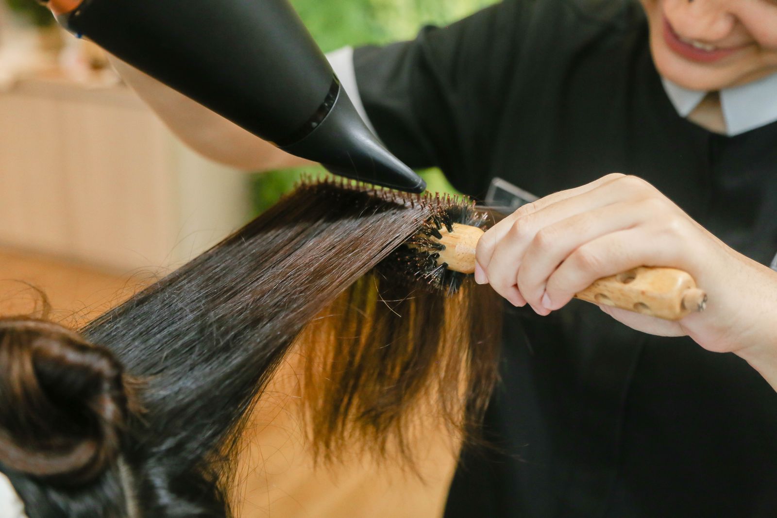 A stylist drying long dark hair with a blow dryer and a round bristle brush