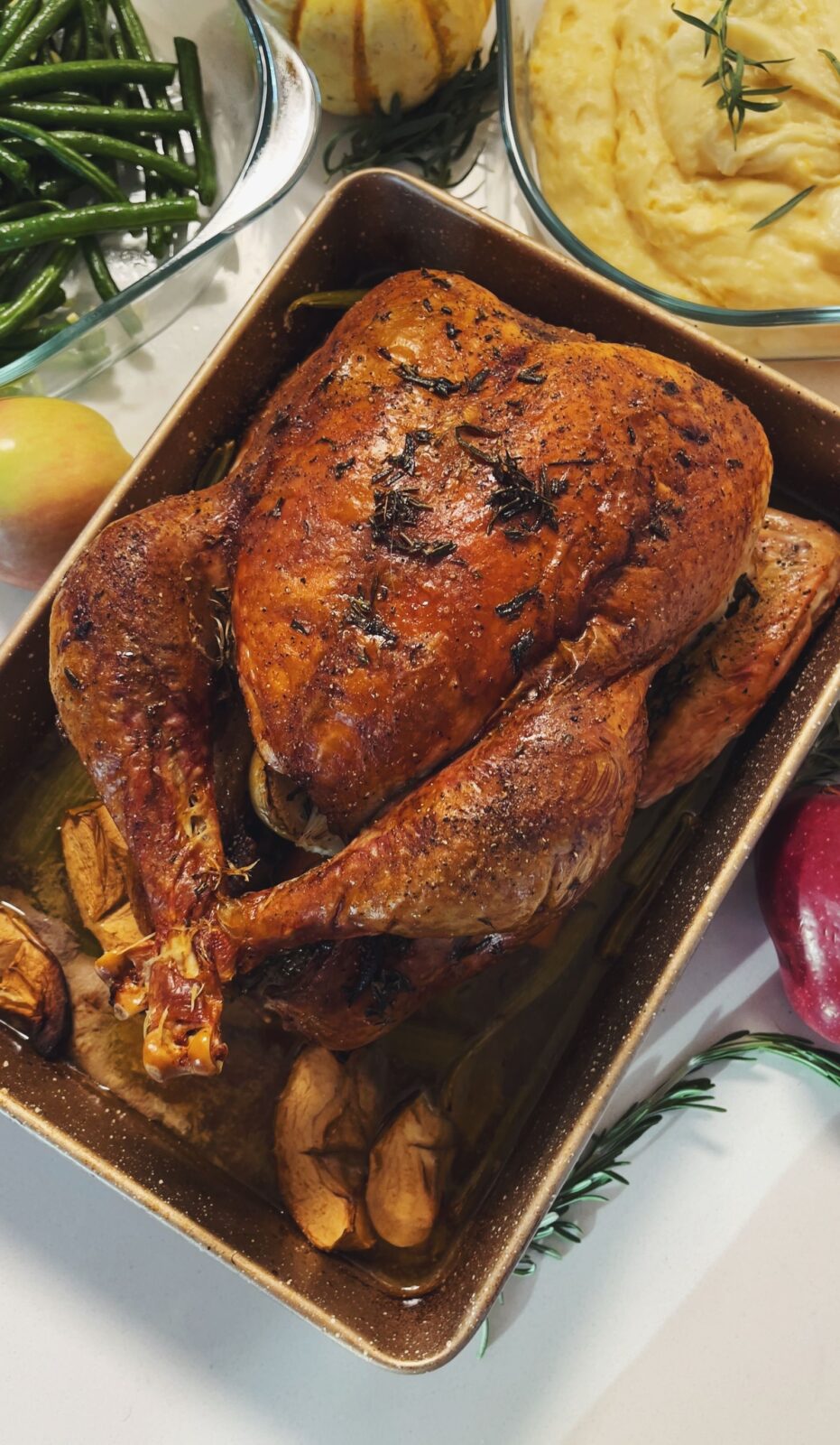 Whole roasted turkey in a rectangular roasting pan beside bowls of green beans and mashed potatoes