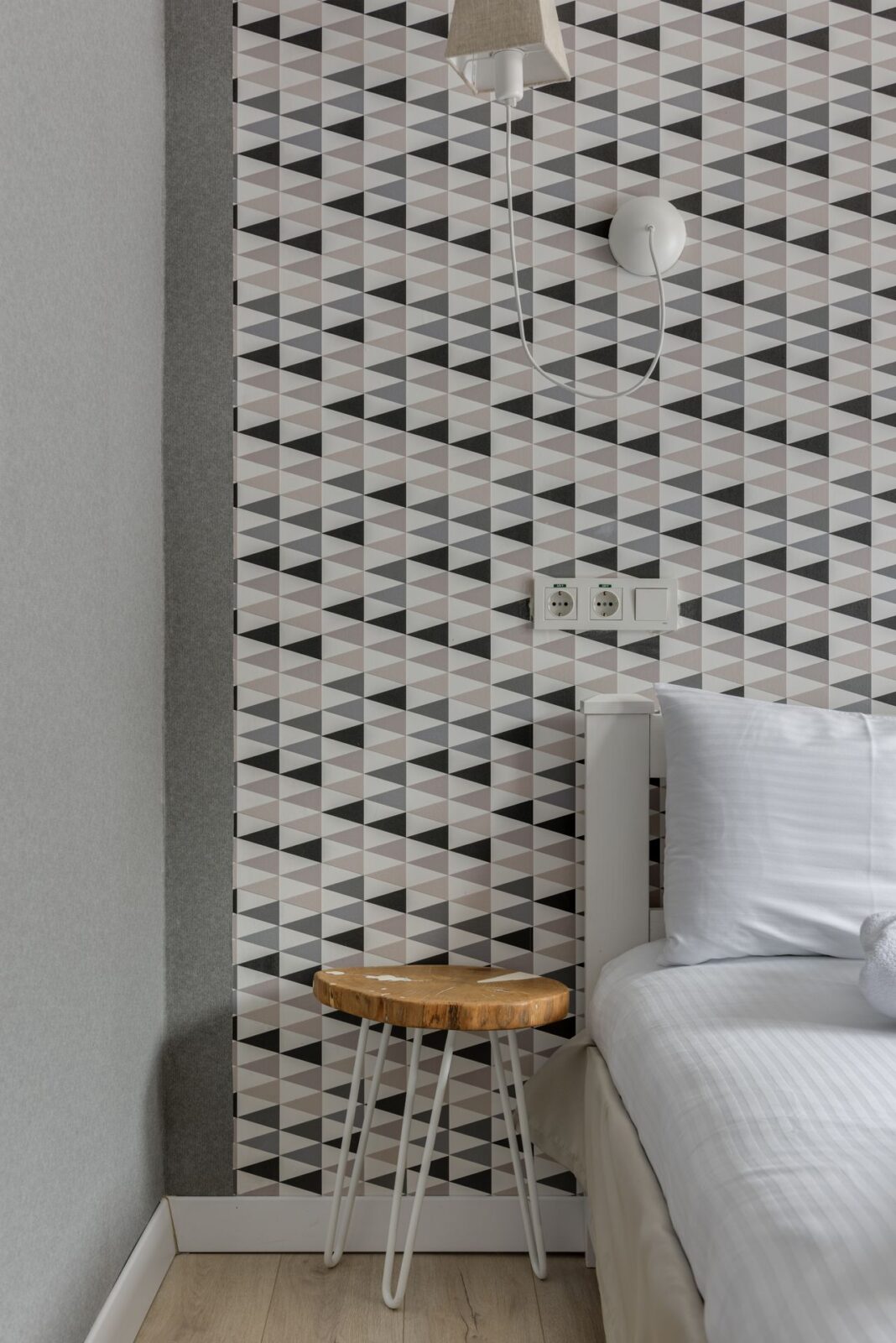 Gray and black triangle-pattern wallpaper behind a bed and a small wooden stool