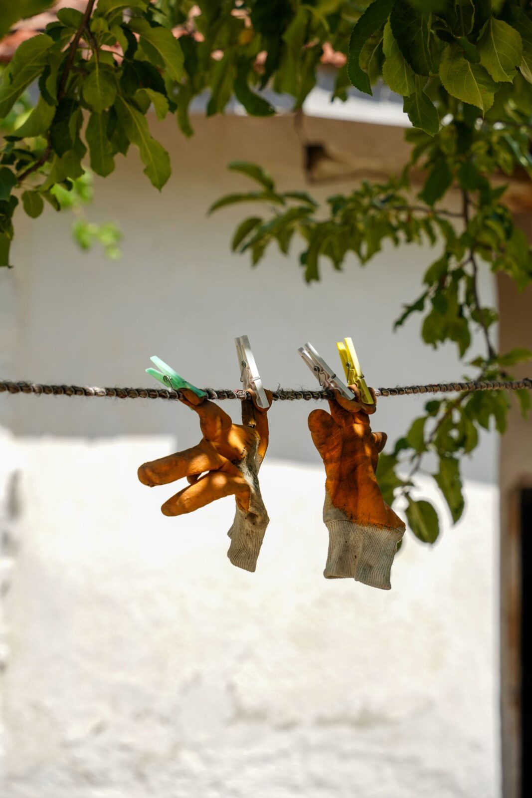 Two worn work gloves hanging from a clothesline with clothespins